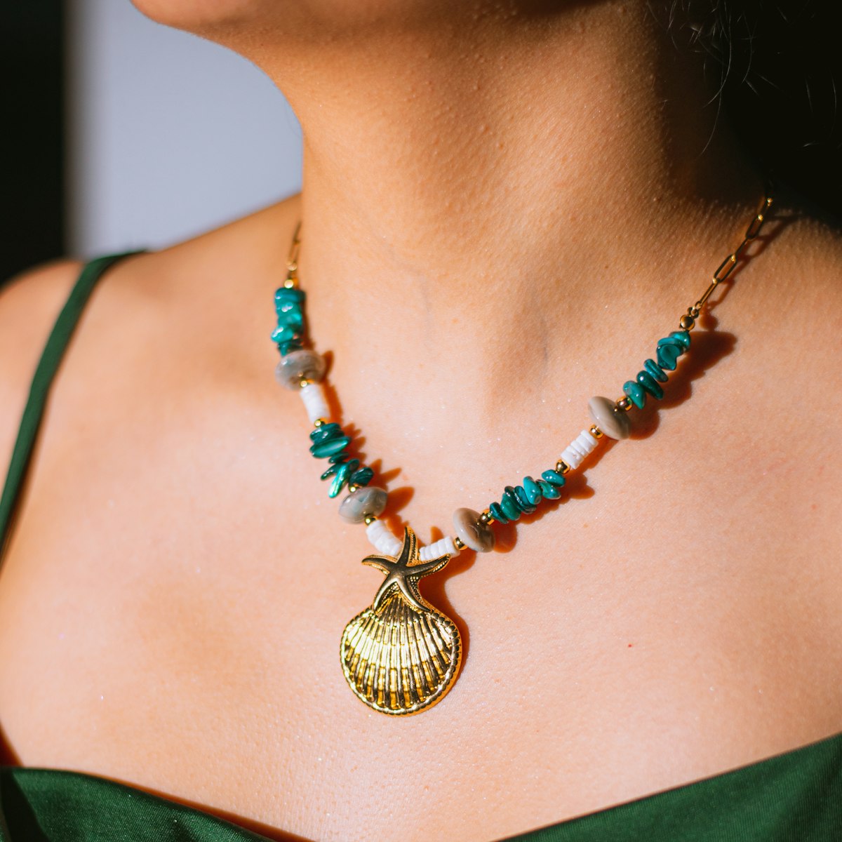 Mulher de vestido verde usando colar de turquesas com pingente dourado